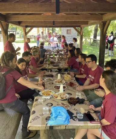 Varias personas comiendo en un merendero mientras unos gaiteros tocan música al fondo