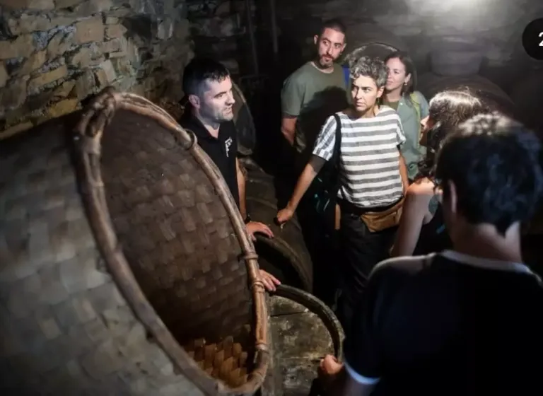 Varias personas escuchando a otra persona que habla junto a varios elementos usados para la producción de vino