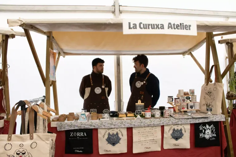 Dos hombres en un puesto de mercadillo llamado "La Curuxa Atelier"